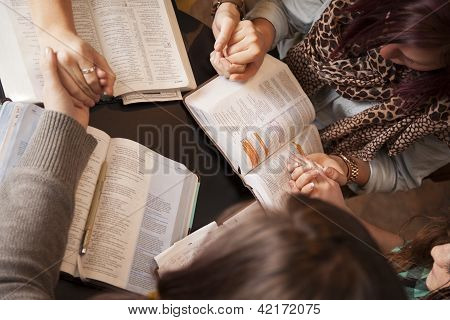 Picture or Photo of A group of young women bow their heads and pray with bibles.
