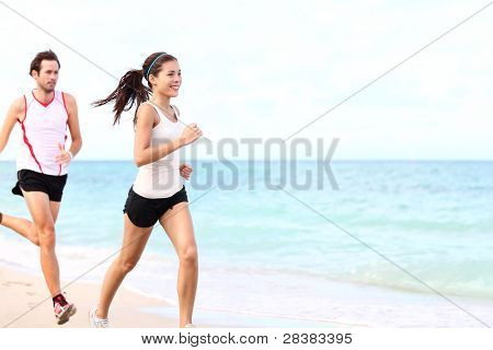 Picture or Photo of Sport - couple running on beach training for marathon run. Young multiracial couple runners, smiling asian female fitness model and caucasian male model.