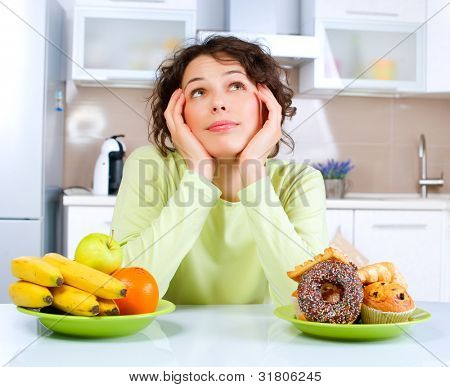 Picture or Photo of Diet. Dieting concept. Healthy Food. Beautiful Young Woman choosing between Fruits and Sweets